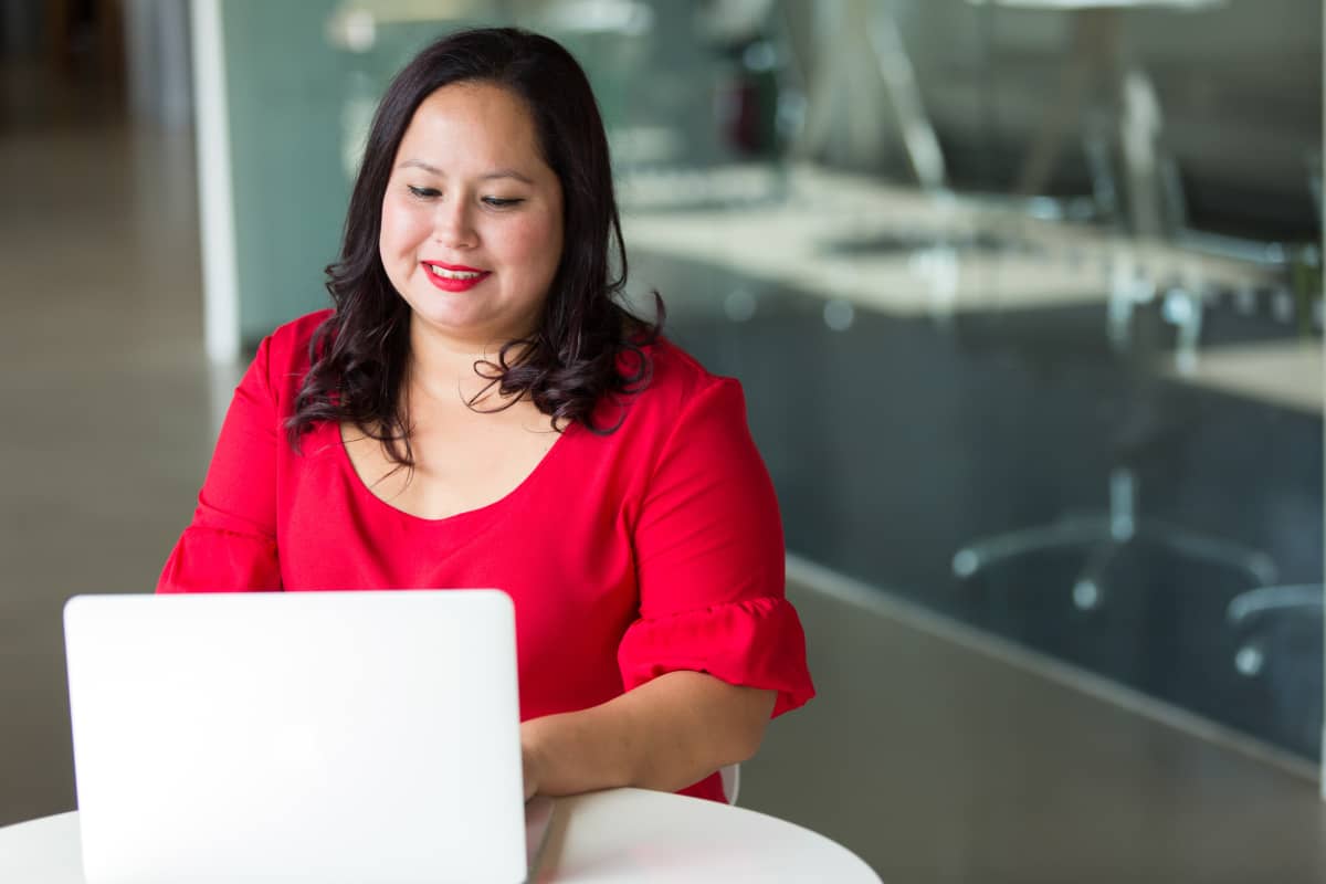 woman-asian-native-on-computer woman in red smiling and typing on a laptop