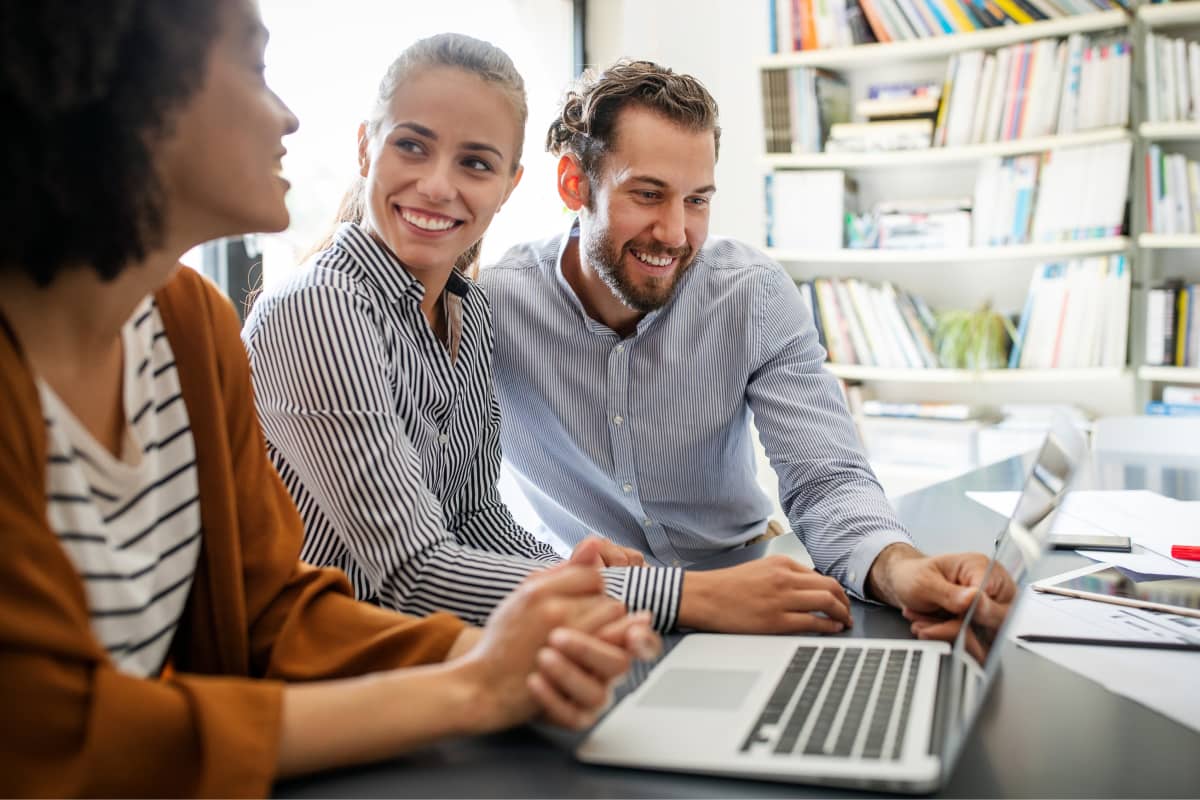 3 people sitting at a laptop smiling